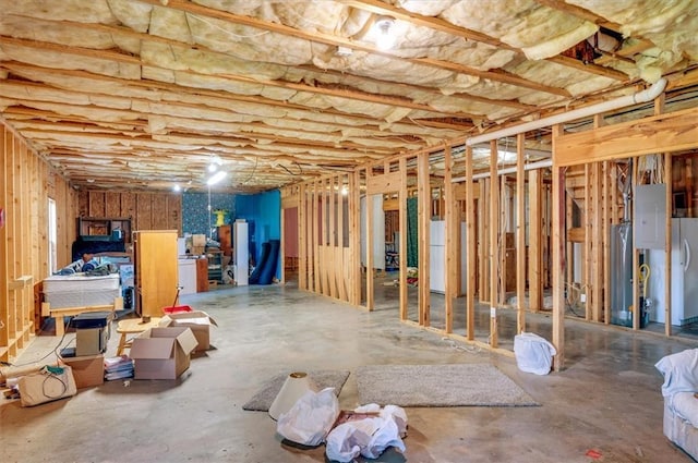 unfinished basement with gas water heater, electric panel, and freestanding refrigerator