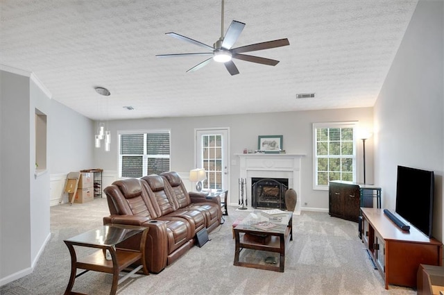 living area with ceiling fan, a textured ceiling, visible vents, a fireplace with flush hearth, and light carpet