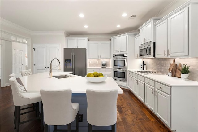 kitchen featuring a kitchen bar, stainless steel appliances, sink, white cabinets, and an island with sink