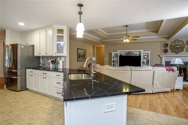 kitchen with a tray ceiling, freestanding refrigerator, white cabinets, a sink, and a peninsula