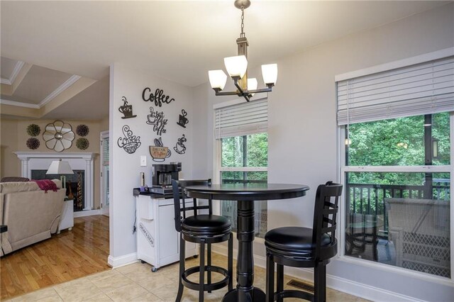 dining space featuring a fireplace, ornamental molding, light tile patterned flooring, a chandelier, and baseboards