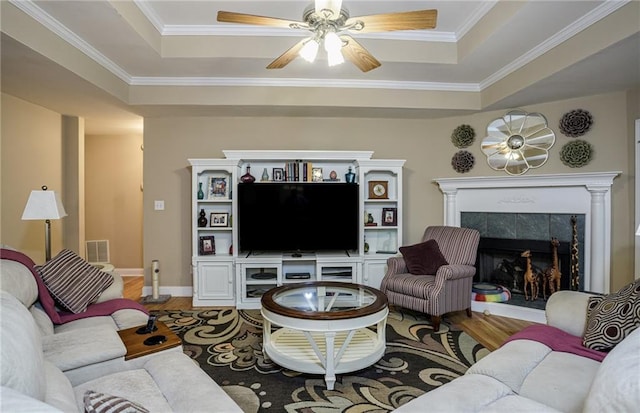 living area with a tray ceiling, a tile fireplace, and wood finished floors