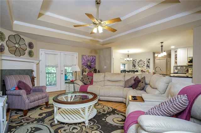 living room featuring ornamental molding, wood finished floors, ceiling fan with notable chandelier, and a raised ceiling