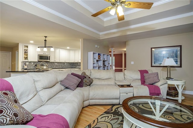 living room featuring a tray ceiling, ornamental molding, light wood-style flooring, and a ceiling fan