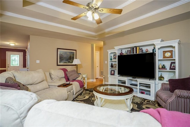 living area with ceiling fan, a raised ceiling, and crown molding