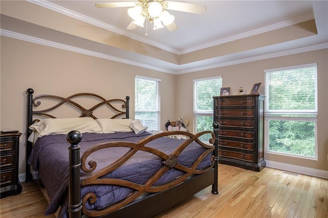 bedroom featuring baseboards, a ceiling fan, a tray ceiling, crown molding, and light wood-style floors