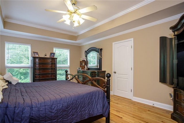 bedroom with light wood-type flooring, a raised ceiling, crown molding, and baseboards