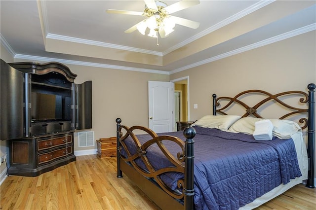 bedroom featuring visible vents, ceiling fan, a tray ceiling, crown molding, and light wood-type flooring