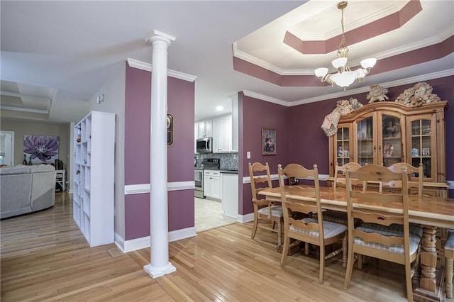 dining room featuring light wood-type flooring, ornate columns, a tray ceiling, and an inviting chandelier