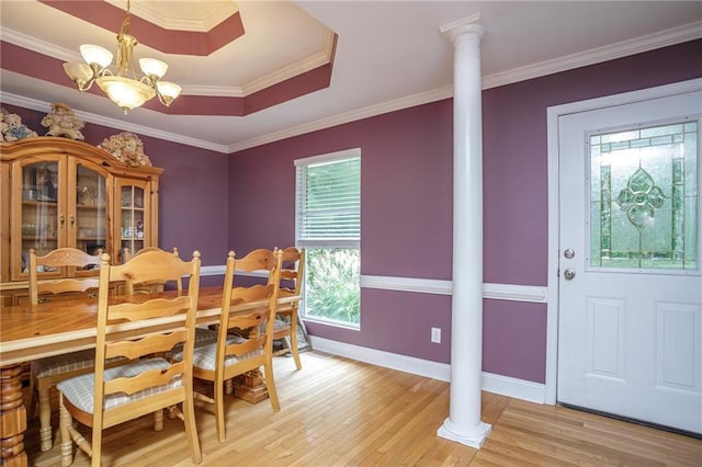 dining area featuring decorative columns, a tray ceiling, crown molding, light wood-style floors, and a chandelier