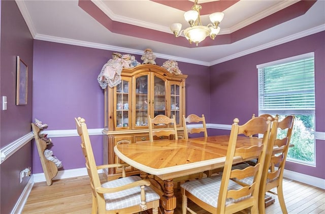 dining area featuring light wood-style flooring, ornamental molding, a raised ceiling, and a notable chandelier