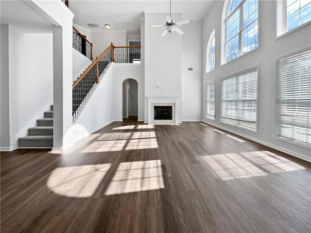 unfurnished living room featuring ceiling fan, a fireplace with flush hearth, wood finished floors, baseboards, and stairway