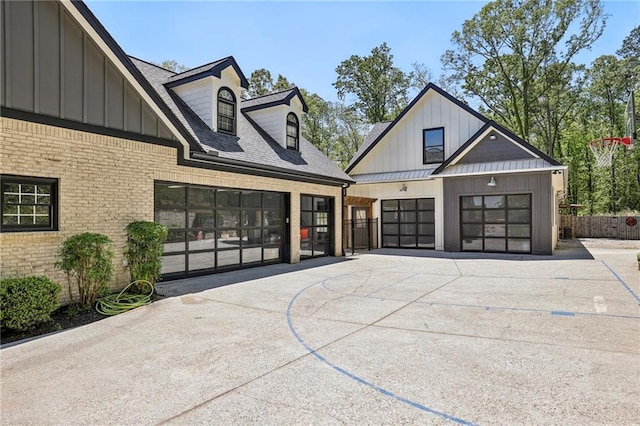 modern farmhouse style home with metal roof, brick siding, a shingled roof, driveway, and board and batten siding