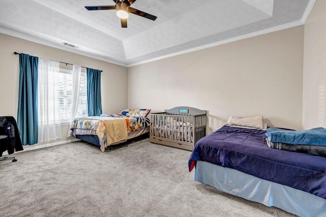 carpeted bedroom with ceiling fan, a tray ceiling, ornamental molding, and a textured ceiling