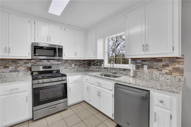 kitchen with a sink, tasteful backsplash, stainless steel appliances, white cabinets, and light tile patterned floors