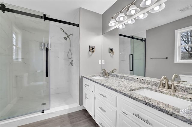 full bath with a sink, visible vents, a marble finish shower, and wood finished floors