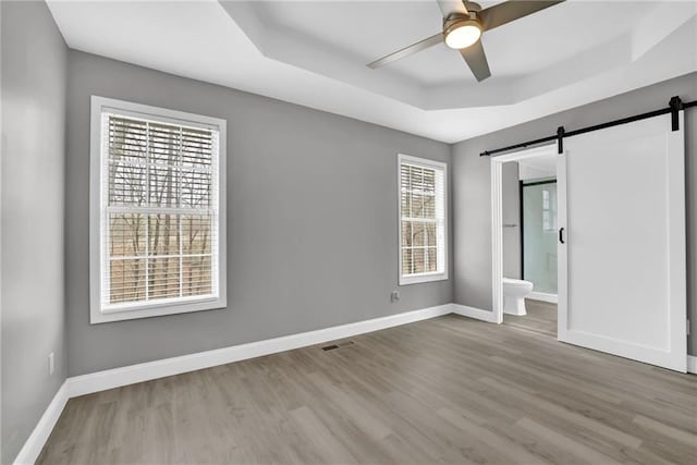 unfurnished bedroom with baseboards, a raised ceiling, a barn door, and wood finished floors