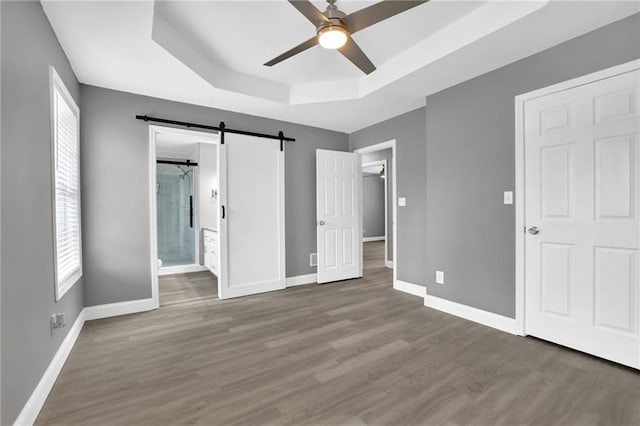 unfurnished bedroom with baseboards, a raised ceiling, a barn door, and wood finished floors