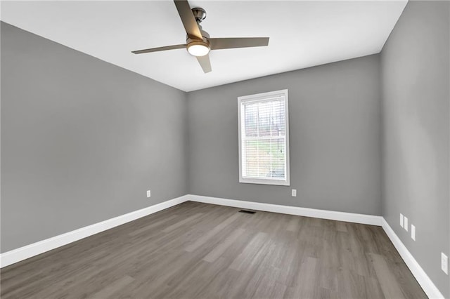 empty room with visible vents, a ceiling fan, baseboards, and wood finished floors