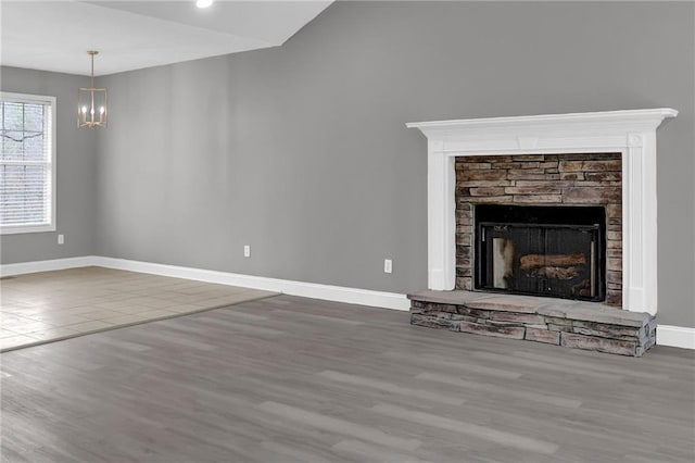 unfurnished living room with baseboards, a notable chandelier, a stone fireplace, and wood finished floors