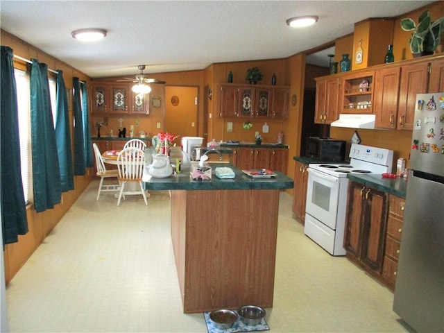 kitchen with stainless steel refrigerator, ceiling fan, a kitchen island with sink, electric range, and vaulted ceiling