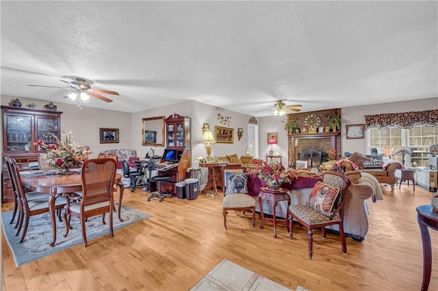 dining room featuring ceiling fan, a fireplace, light hardwood / wood-style floors, and a textured ceiling