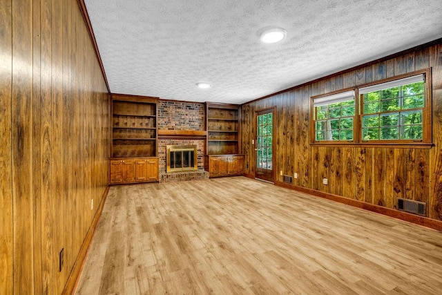 2775 Doaks Run Ct, Tucker, GA 30084 - unfurnished living room with a brick fireplace, wood walls, light wood-type flooring, a textured ceiling, and built in shelves