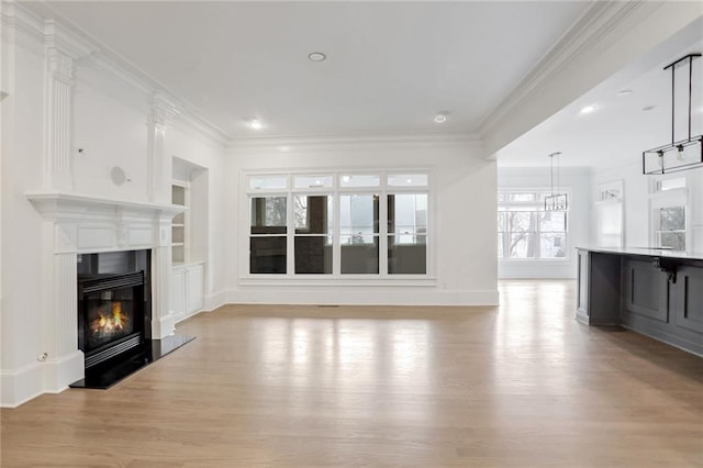 unfurnished living room with light wood finished floors, a glass covered fireplace, built in shelves, and crown molding