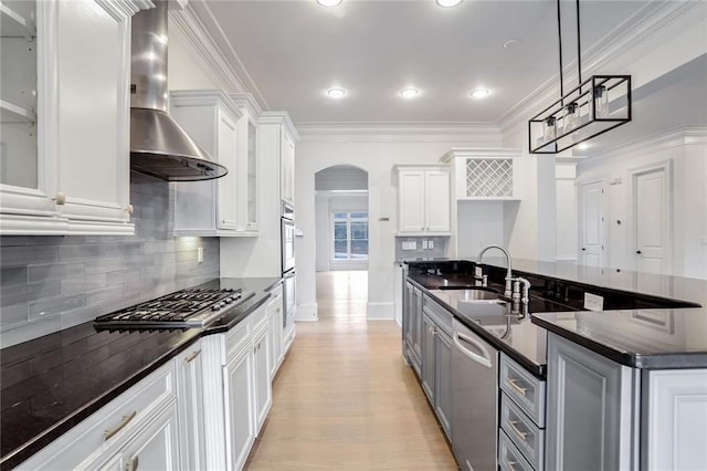 kitchen featuring gray cabinetry, ornamental molding, arched walkways, appliances with stainless steel finishes, and wall chimney exhaust hood