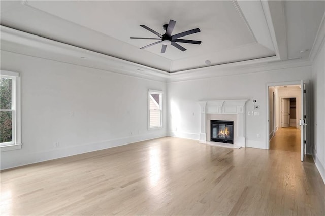 unfurnished living room with a glass covered fireplace, ceiling fan, a tray ceiling, and wood finished floors