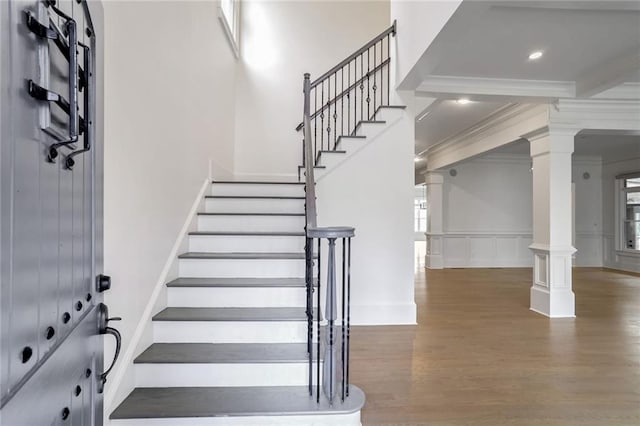 staircase featuring wood finished floors, ornate columns, recessed lighting, ornamental molding, and a decorative wall