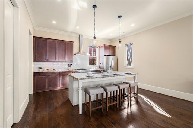 kitchen featuring stainless steel refrigerator with ice dispenser, decorative backsplash, wall chimney range hood, an island with sink, and a kitchen bar