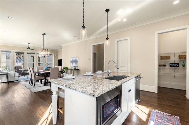 kitchen featuring a sink, ornamental molding, dark wood-style floors, stainless steel microwave, and decorative light fixtures