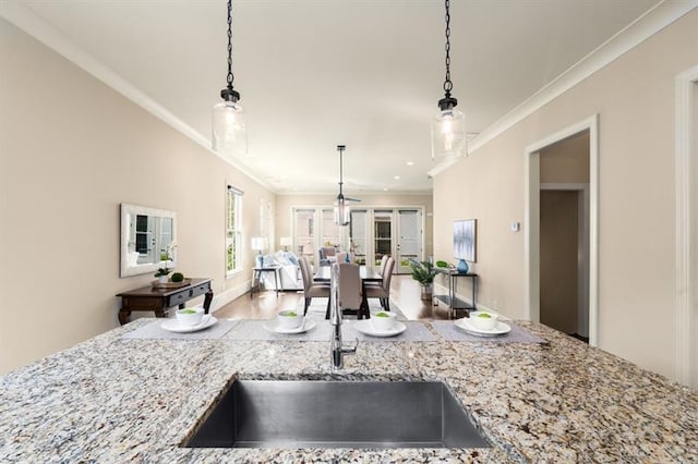 kitchen featuring crown molding, open floor plan, a sink, and light stone countertops