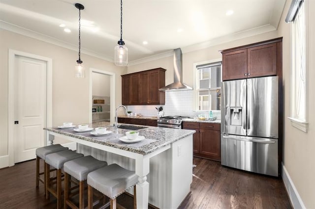 kitchen with a sink, appliances with stainless steel finishes, wall chimney exhaust hood, dark wood finished floors, and a center island with sink