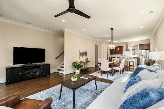 living room featuring wood finished floors, crown molding, baseboards, and stairs