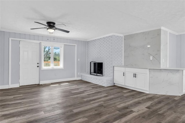 unfurnished living room featuring dark wood-style floors, a brick fireplace, a textured ceiling, and ornamental molding