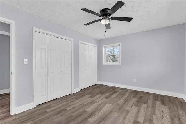 unfurnished bedroom featuring baseboards, two closets, wood finished floors, and a textured ceiling