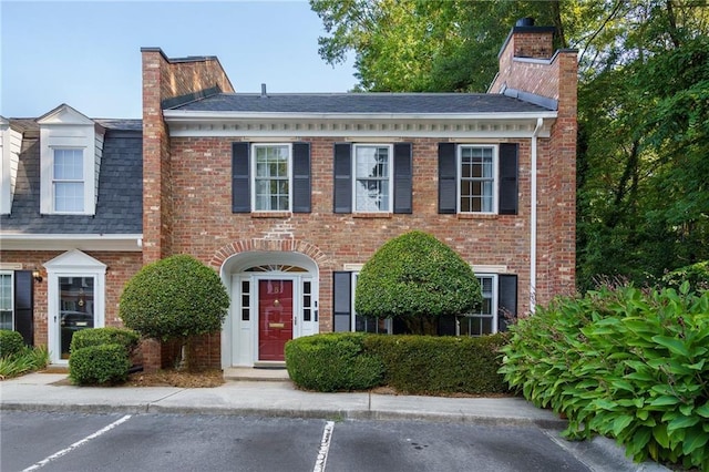 view of front facade featuring uncovered parking, brick siding, and a chimney