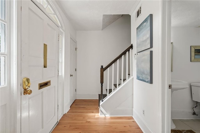 entrance foyer with stairway, light wood-type flooring, visible vents, and baseboards