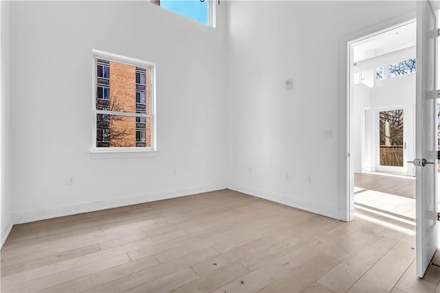 unfurnished room with light wood-type flooring, a wealth of natural light, and a towering ceiling