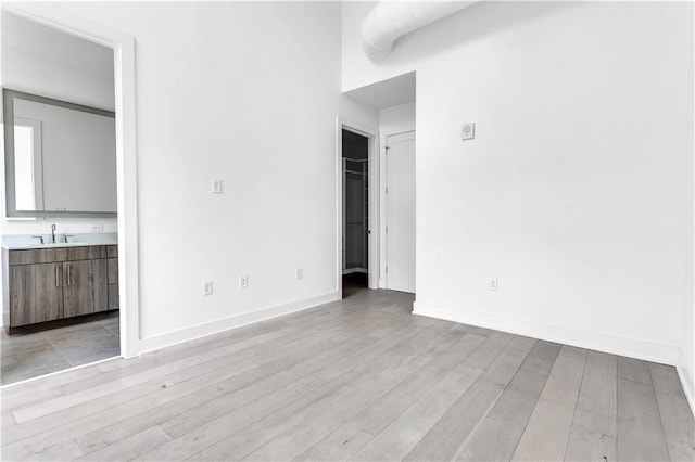 unfurnished bedroom with ensuite bathroom, sink, and light hardwood / wood-style flooring