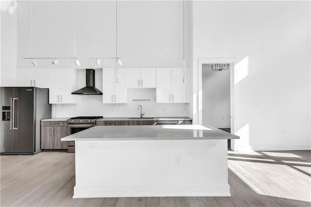 kitchen with a center island, stainless steel appliances, wall chimney range hood, white cabinets, and light wood-type flooring