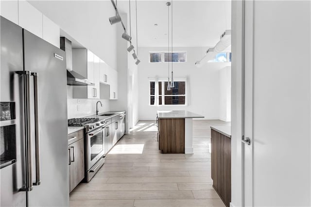 kitchen featuring a kitchen island, high end appliances, white cabinetry, and hanging light fixtures