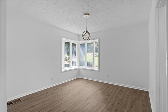 unfurnished room with a textured ceiling, dark hardwood / wood-style floors, and a notable chandelier