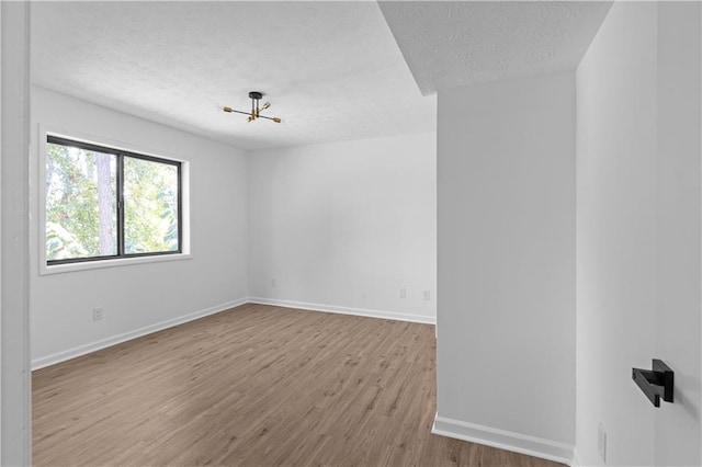 spare room featuring an inviting chandelier, light wood-type flooring, and a textured ceiling