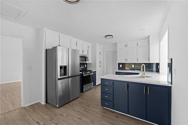 kitchen featuring blue cabinets, white cabinets, sink, appliances with stainless steel finishes, and light wood-type flooring