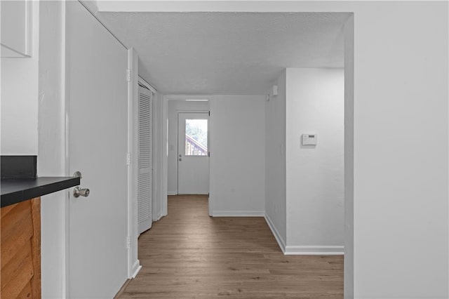 hallway with light wood-type flooring and a textured ceiling