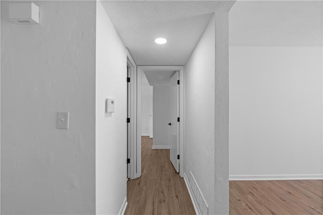 hall featuring light wood-type flooring and a textured ceiling