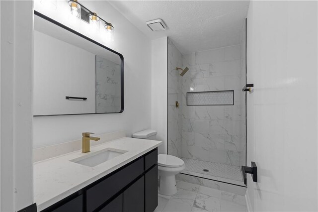 bathroom with a textured ceiling, a tile shower, vanity, and toilet